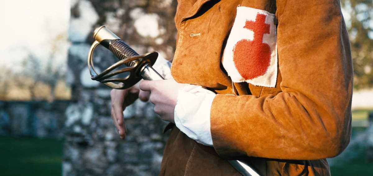 Détail d'un costume vendéen : main tenant un sabre, Sacré-Cœur cousu sur la veste.