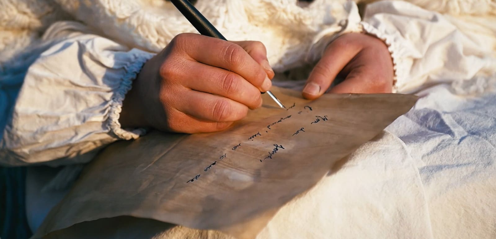 Une main écrit une lettre à la plume, en costume d'époque.